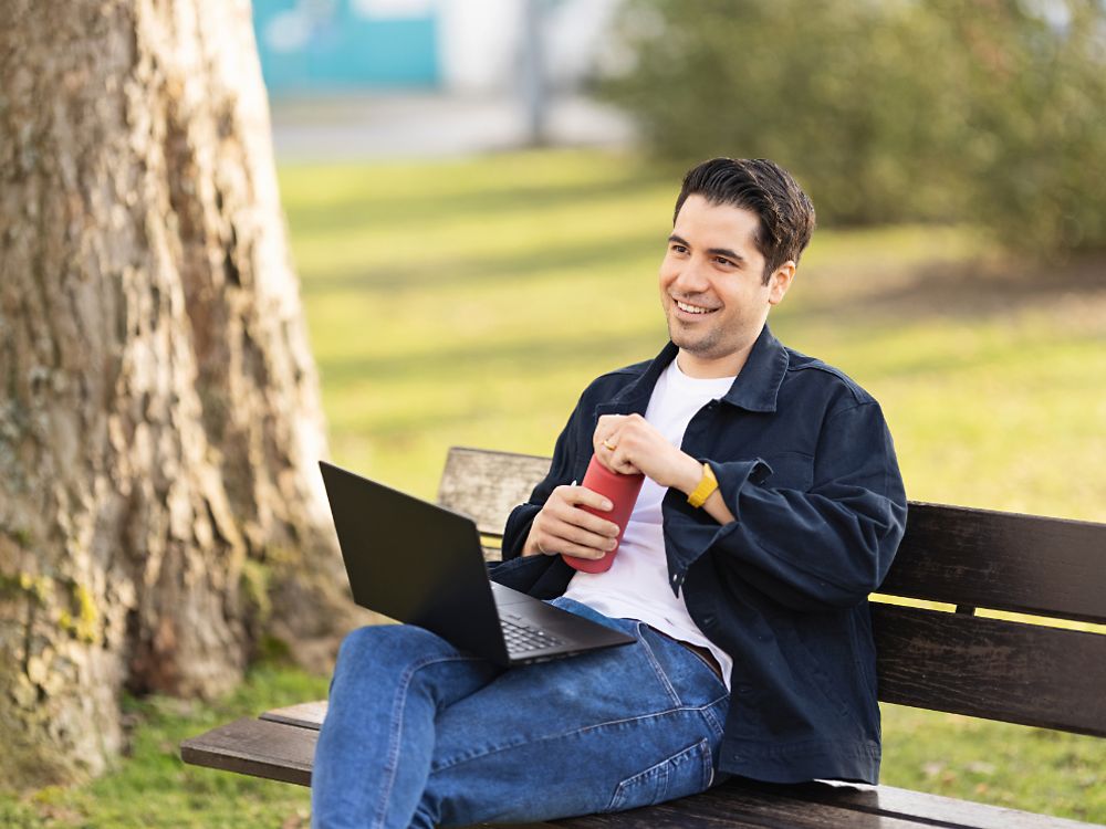 Zamestnanec spoločnosti Henkel sedí na lavičke v parku a pracuje s laptopom.