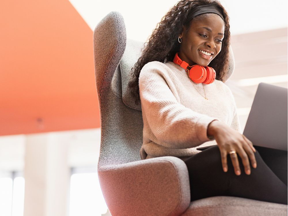 Zamestnankyňa spoločnosti Henkel sedí v pohodlnom kresle s laptopom na kolenách. Usmieva sa.