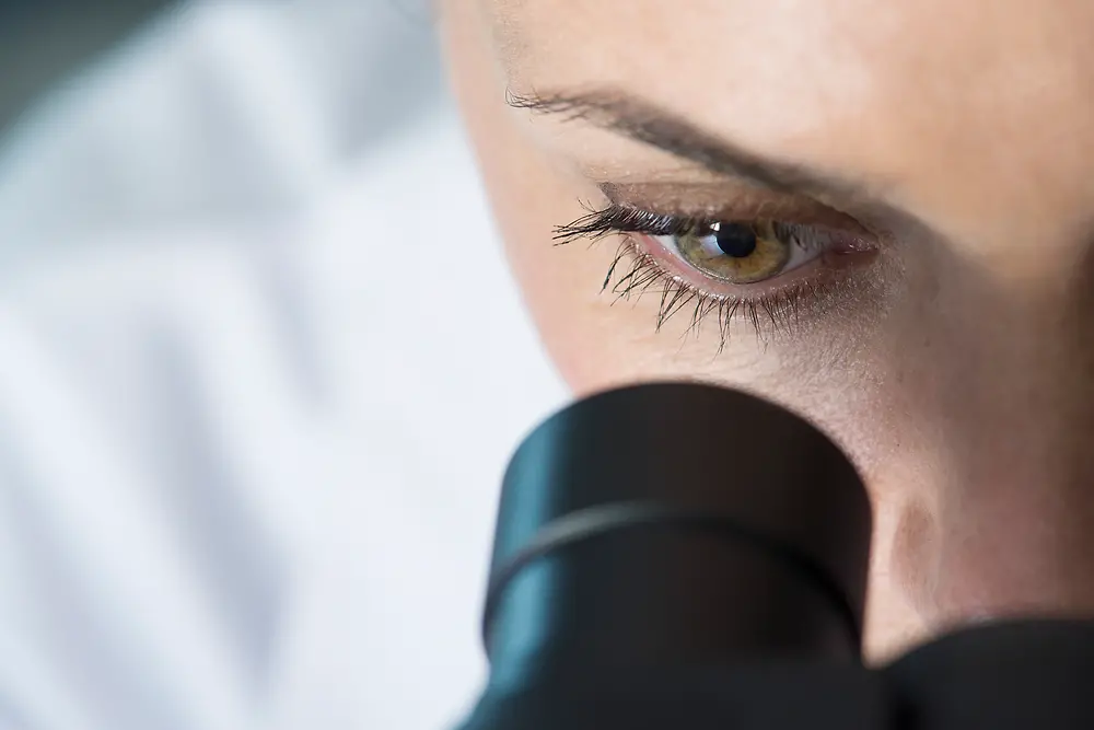 Oko ženy hledící do mikroskopu