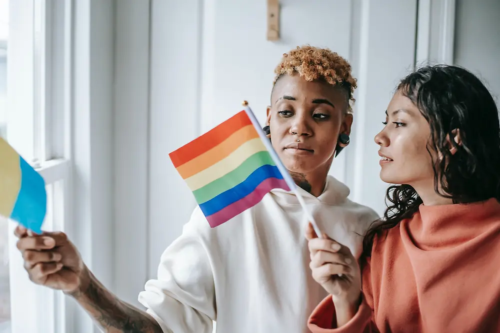 Dvě ženy spolu hovoří a přitom drží vlajku LGBTQ+.