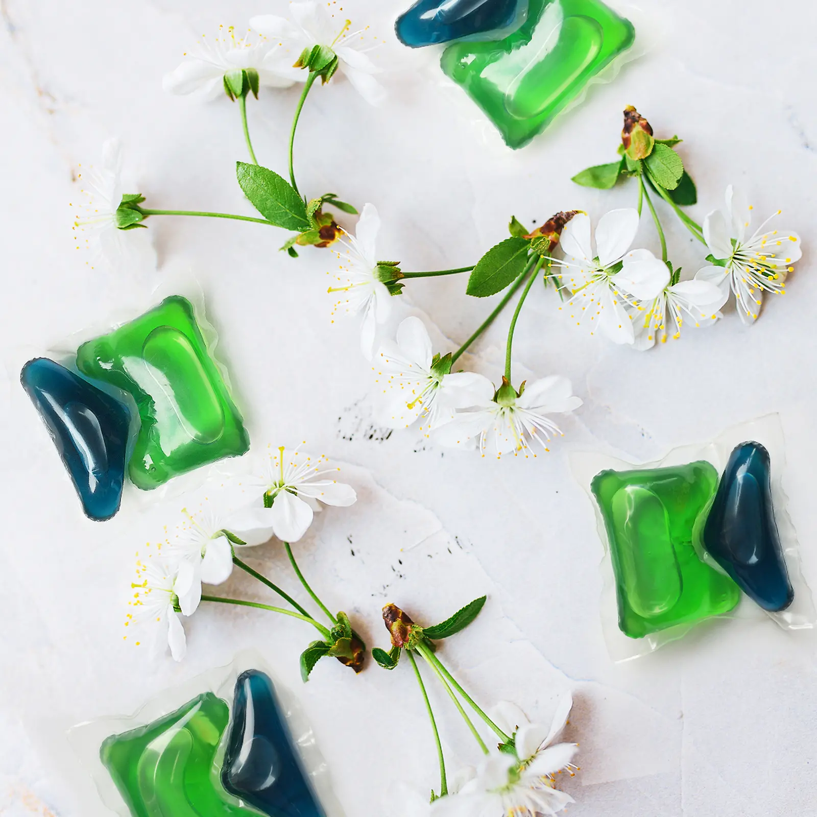 Dvě zelené a modré Henkel Persil tablety s třešňovými květy okolo