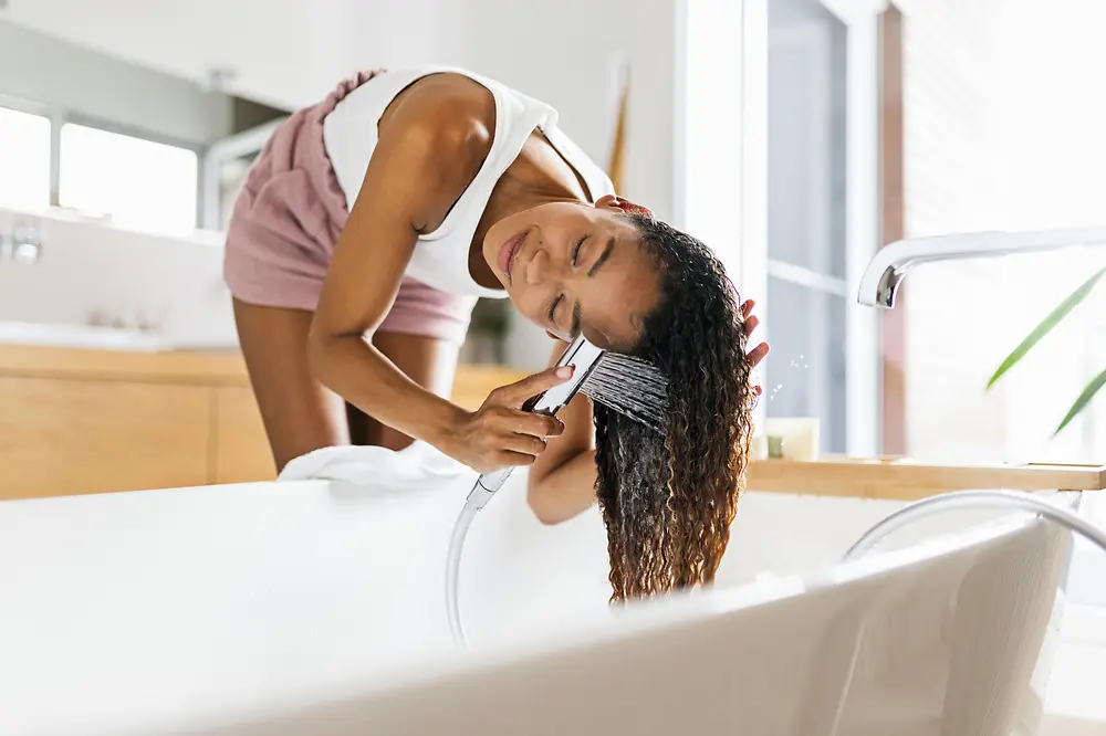 Žena v koupelně myje své hnědé dlouhé vlasy ve vaně