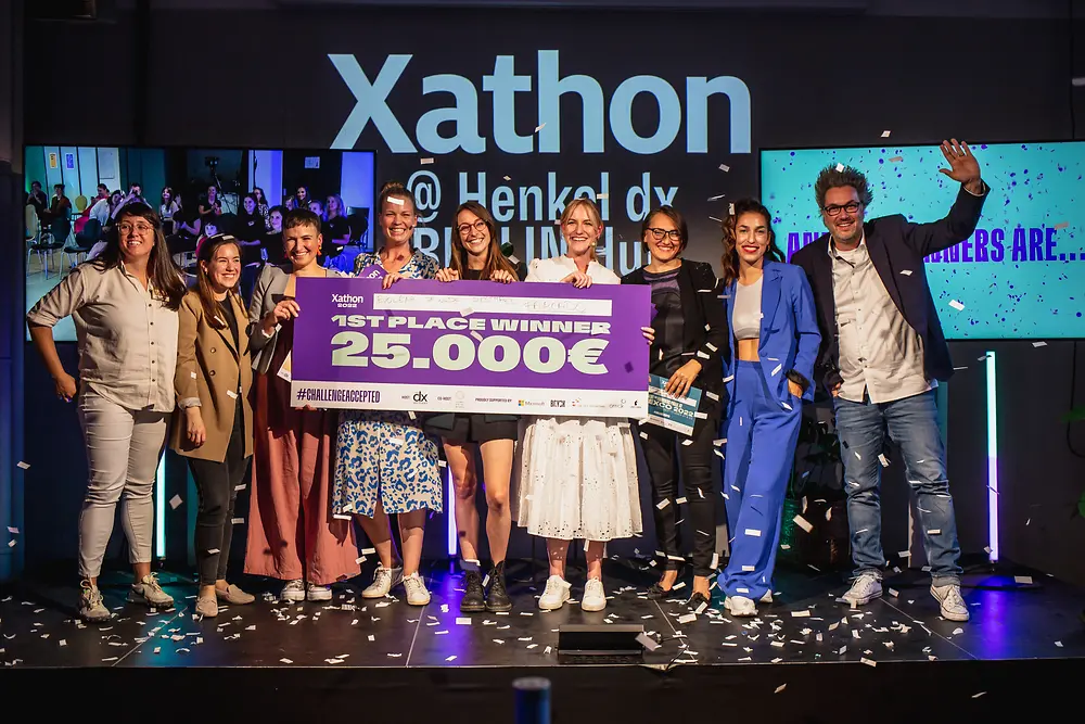 Xathon winners from last year are standing on the stage together with representatives of Henkel dx Ventures celebrating and holding a symbolic cheque of 25,000 euros. 