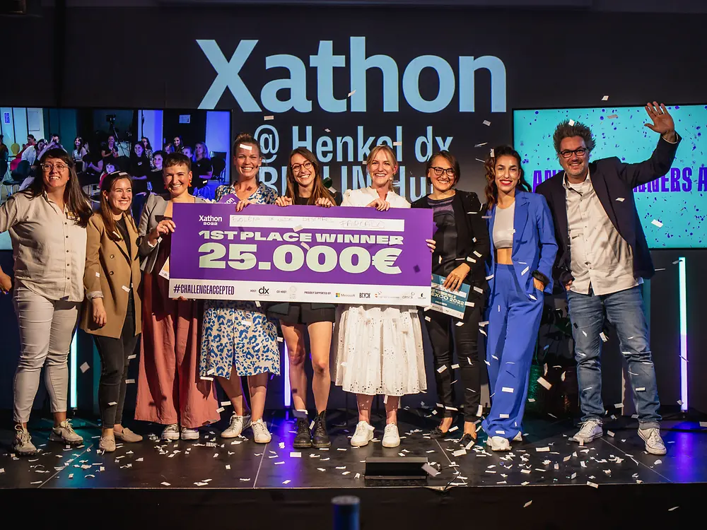 Xathon winners from last year are standing on the stage together with representatives of Henkel dx Ventures celebrating and holding a symbolic cheque of 25,000 euros. 