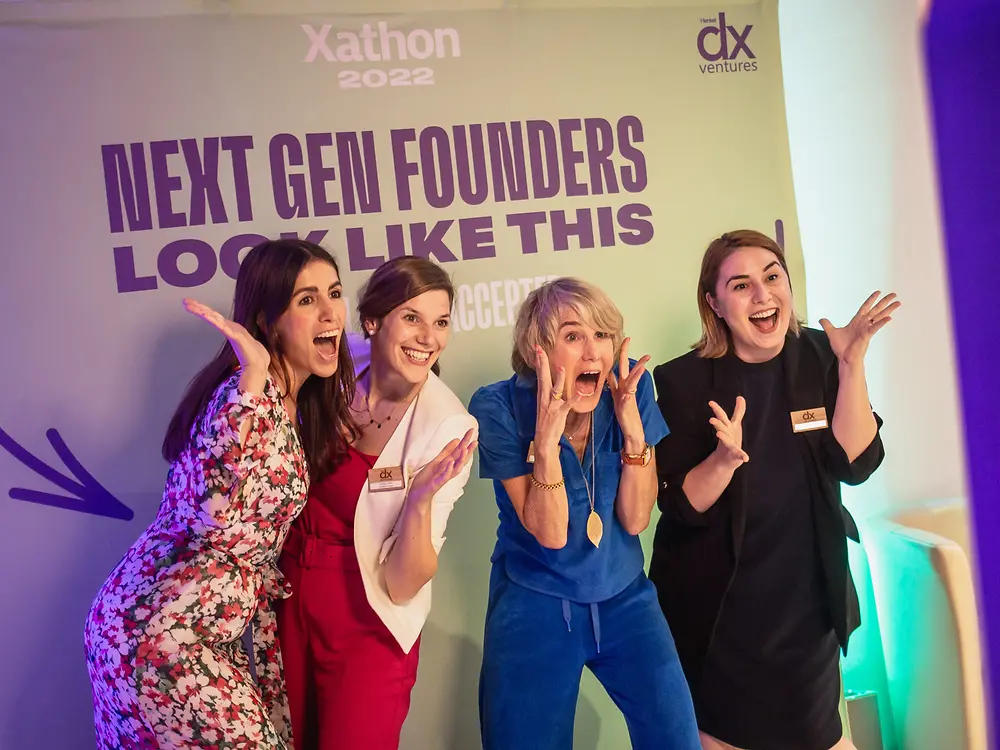 Four female entrepreneurs are standing in front of a photo wall which has 
