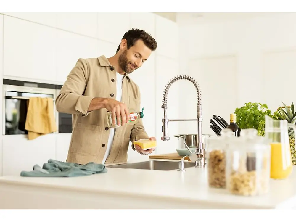 Man stands at the sink and pours Pril onto a sponge.
