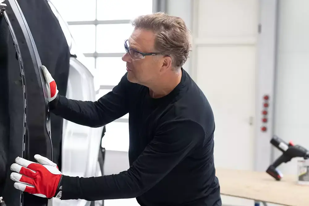 Technik opravující nebo servisující dveře vozidla v automobilové dílně.